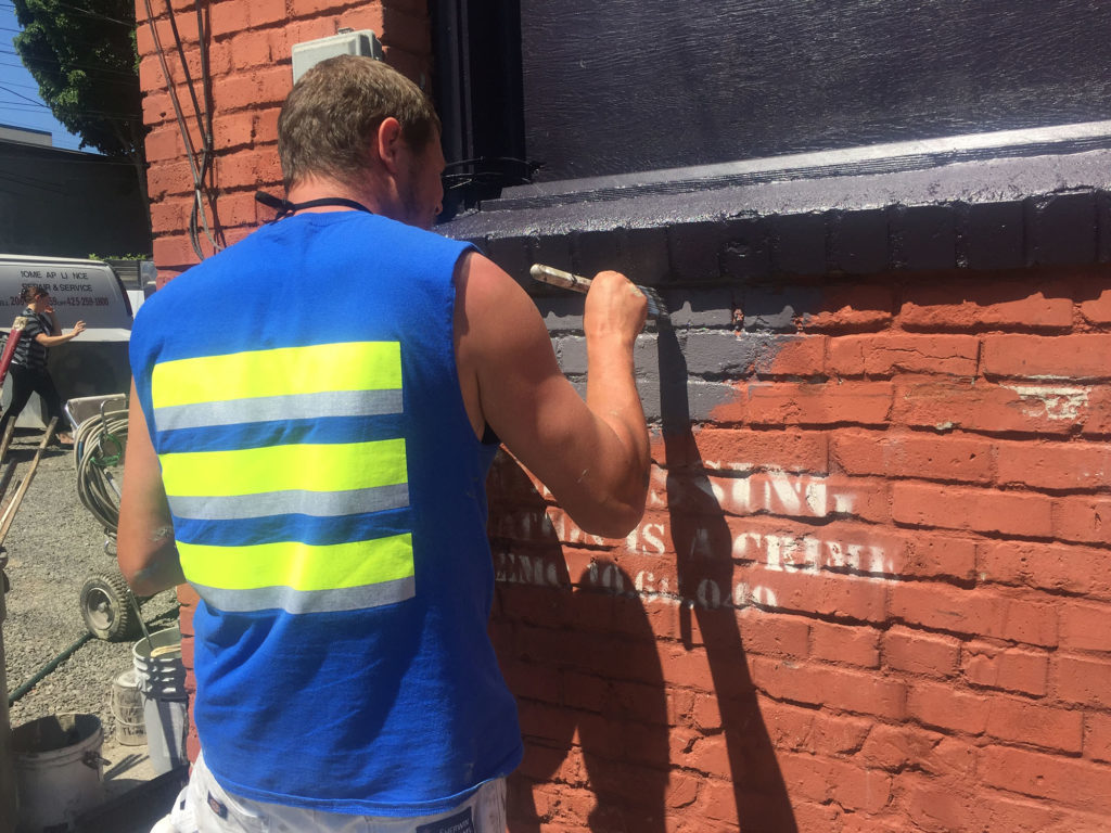 Commercial painting contractor applying exterior paint to a brick commercial building in Western Washington.
